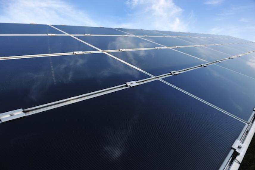 Solar panels reflecting sky, under a blue, partly cloudy day.