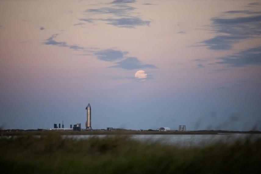 Sunset sky with a rocket on distant horizon over grassy field and water.