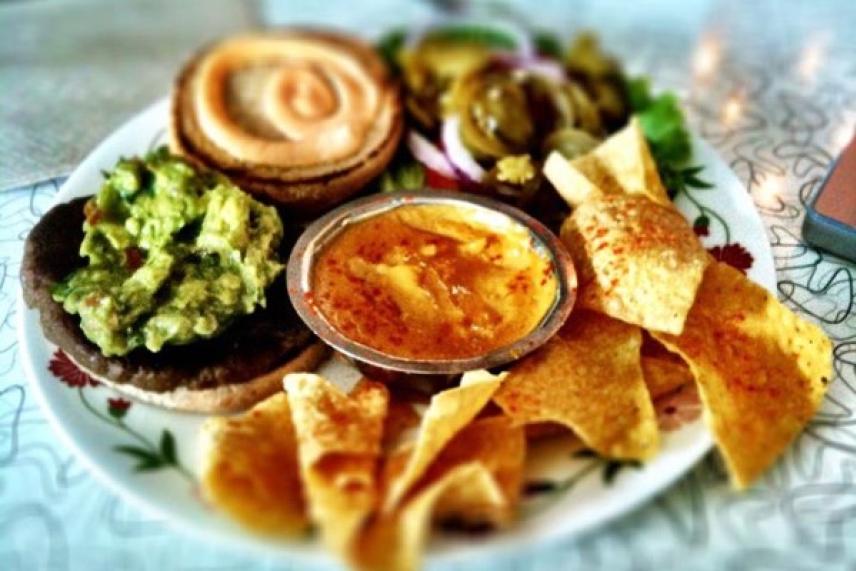 Platter with guacamole, chips, hummus, jalapeños, and pastries.