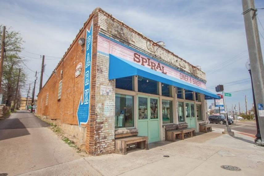 Brick corner building with blue awning and large windows under a clear sky.