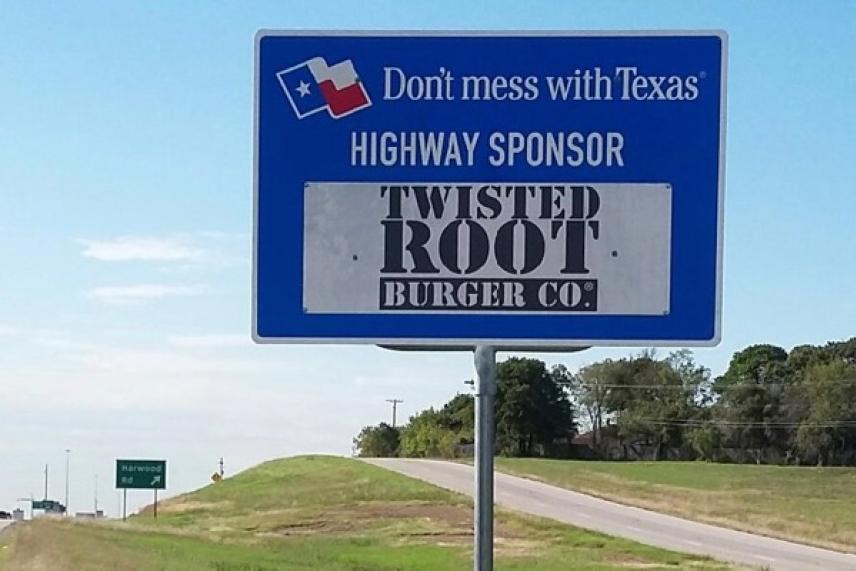 Texas highway sign with sponsor logo on roadside.