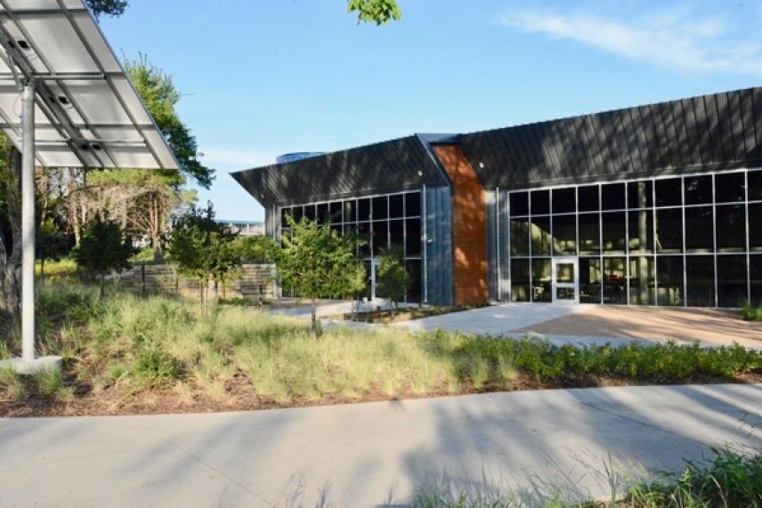 Modern building with large windows, surrounded by greenery and a clear blue sky.