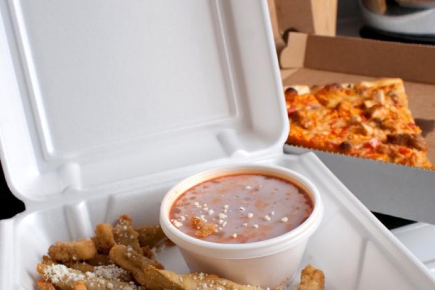 Takeout box with fries and dip, pizza slice in background.