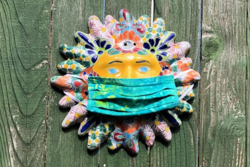 Colorful sun mask on wood wall, wearing a green face mask.