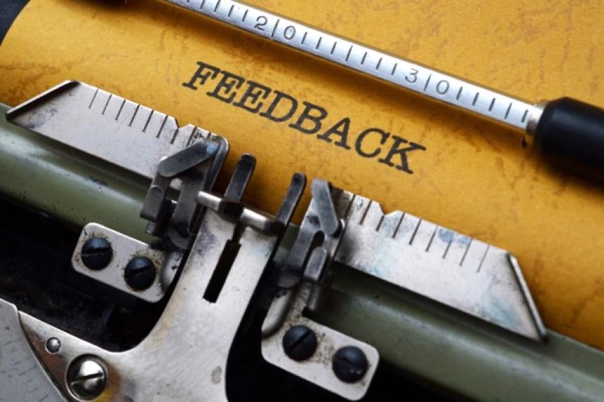 Typewriter with "FEEDBACK" on yellow paper, focusing on typebars.