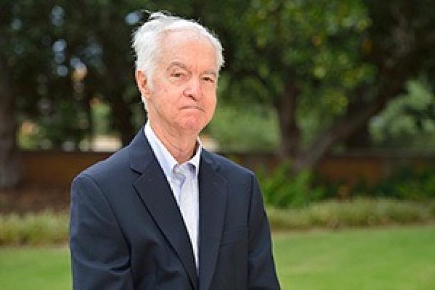 Elderly man in a suit standing outdoors in a garden.
