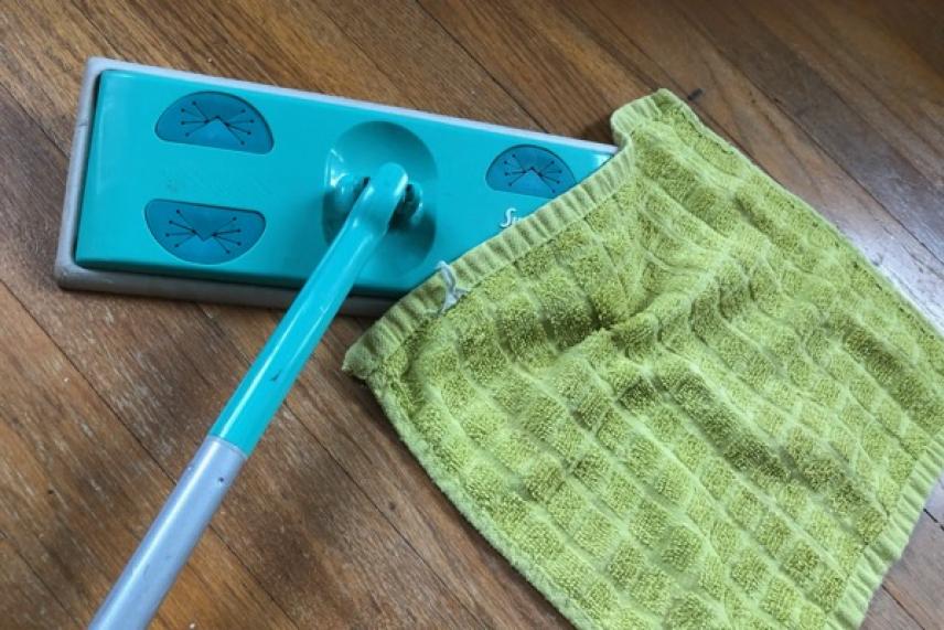 Flat mop with green cloth on wood floor.