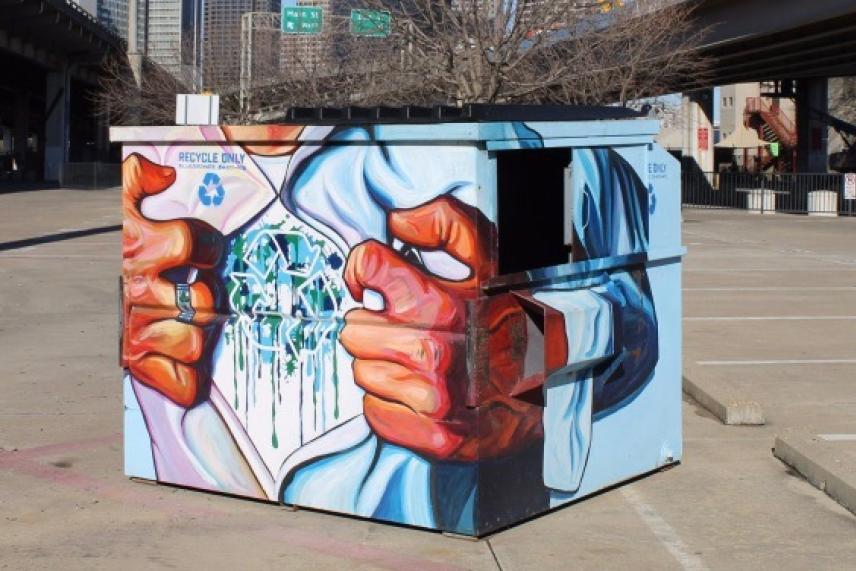 Colorful mural on a dumpster, depicting hands tearing open a shirt to reveal recycling symbols.