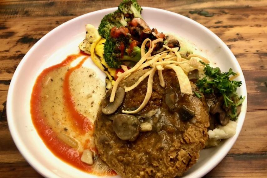 Plate of vegetables, mashed potatoes, and patty garnished with sauce and herbs.