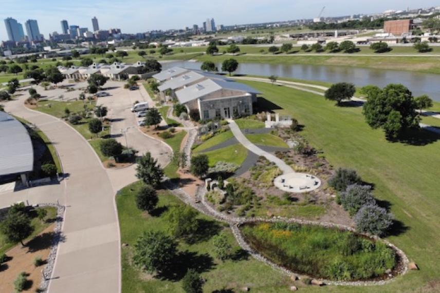 Aerial view of a park with gardens, pathways, and distant city skyline.