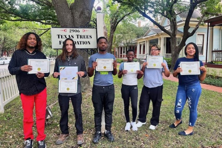 Six people standing outdoors, smiling, holding certificates.