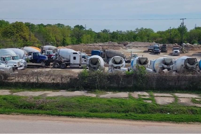 Concrete trucks parked in a lot with trees in the background.