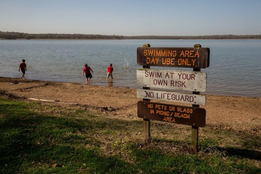 Lake with swimmers and a sign warning of no lifeguard.