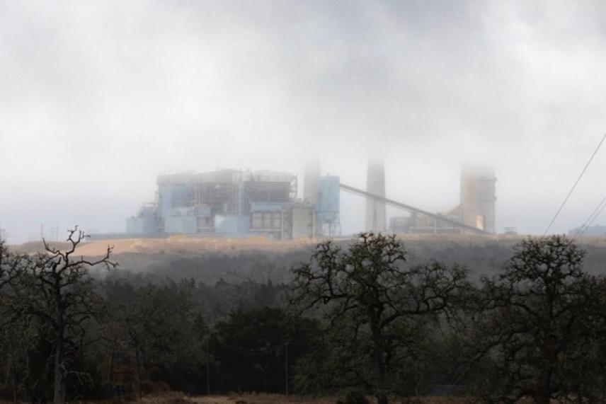 Factory obscured by mist, surrounded by trees, under a cloudy sky.