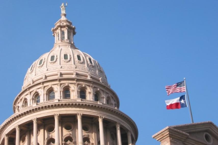 Texas Capitol dome with U.S. and Texas flags against a clear blue sky.