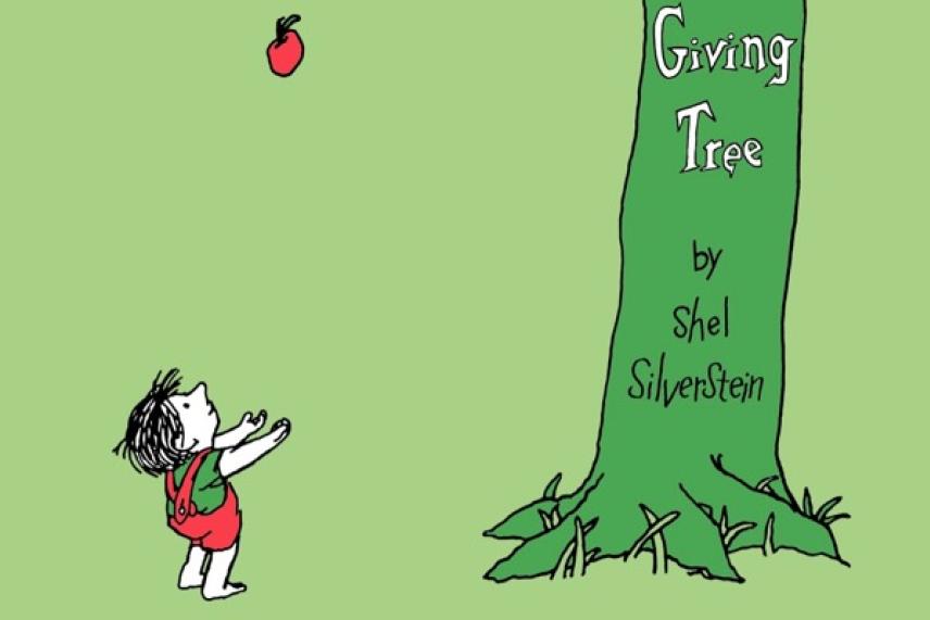Child reaching for an apple near a large green tree.