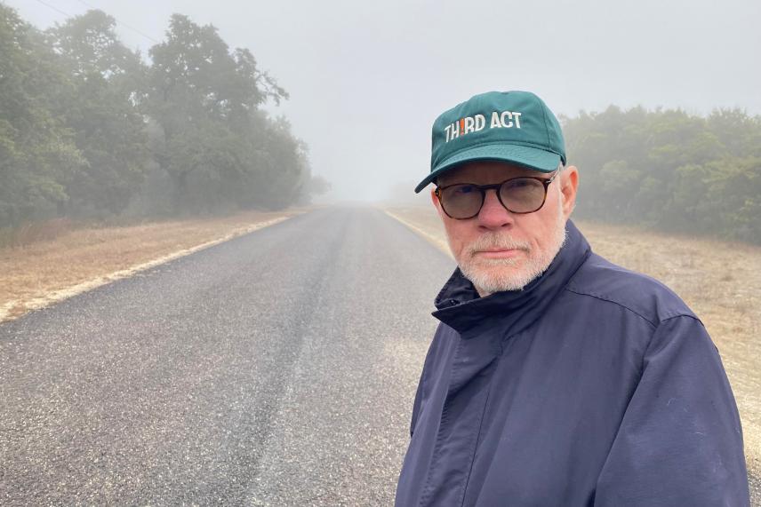 Man in a jacket and cap standing on a foggy road.
