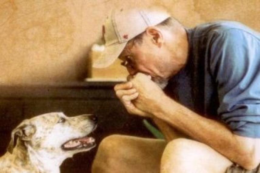 Man in cap playing harmonica to attentive spotted dog.