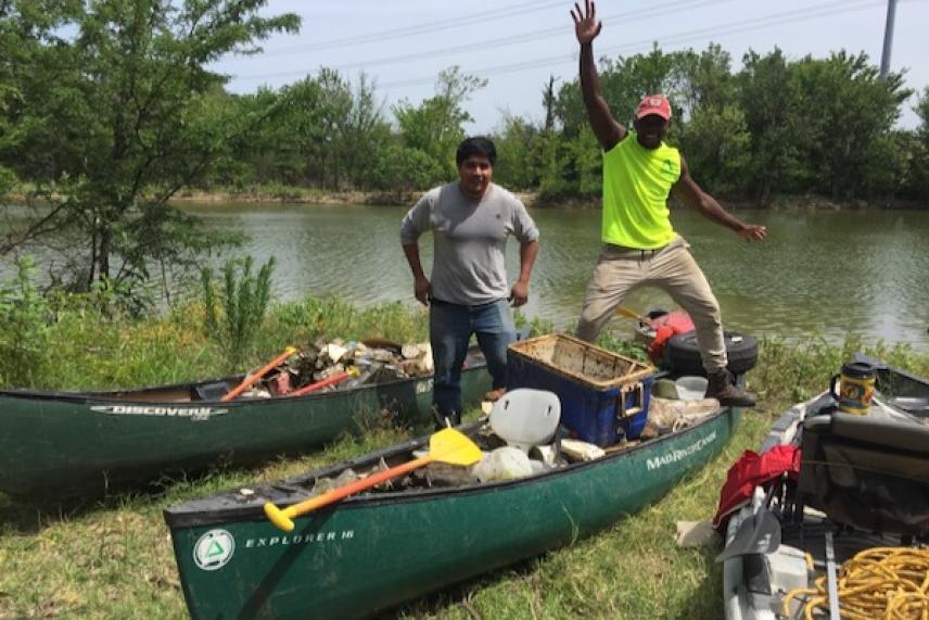 Two people pose with canoes full of supplies by a river.