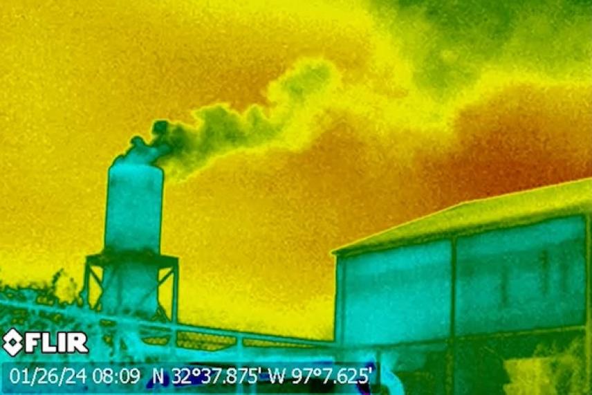 Thermal image of smoke billowing from a smokestack against a vivid yellow and orange sky.