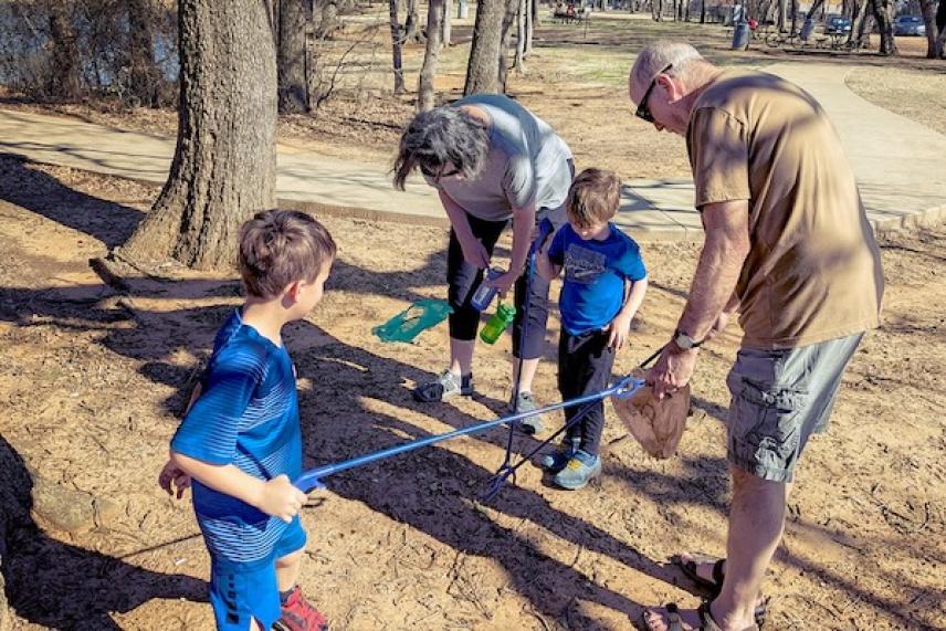 Adults and children picking up litter in a sunny park.