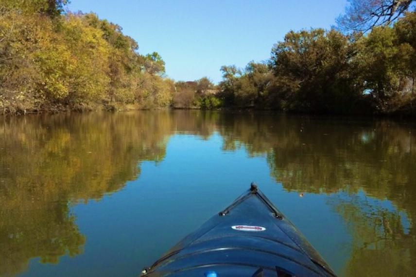 Kayak gliding on calm river, surrounded by autumn trees under a clear blue sky.
