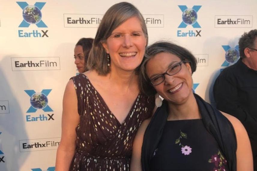 Two women smiling at an outdoor event with a branded backdrop.