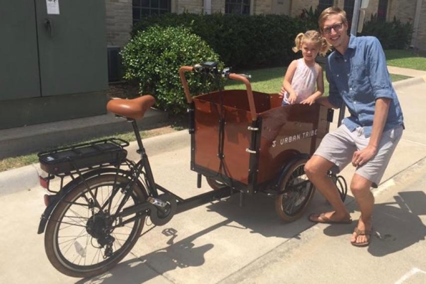 Man and child smiling beside a cargo bike on a sunny day.