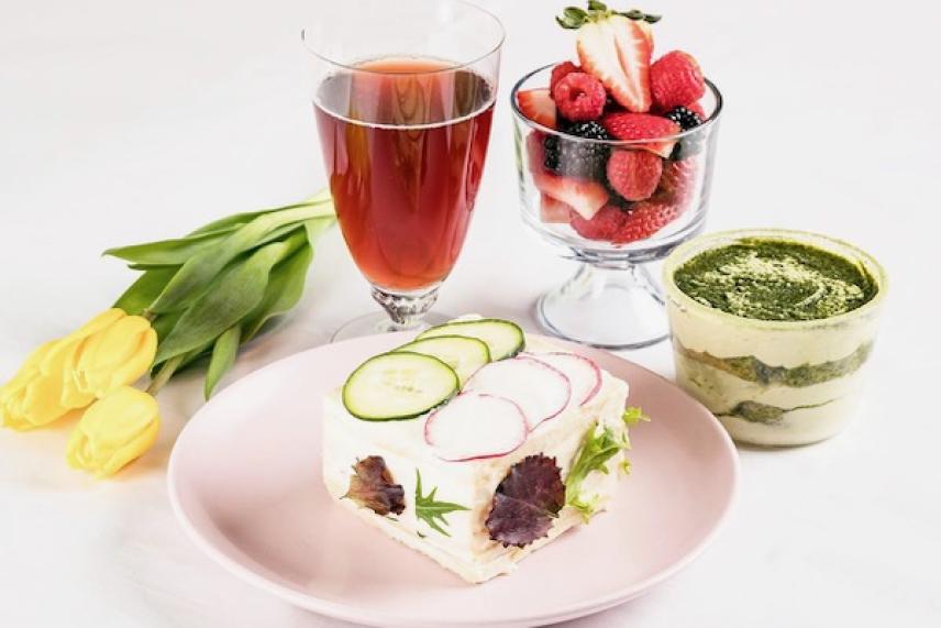 Slice of sandwich cake, tea, berries, matcha dessert, and yellow tulips on a table.
