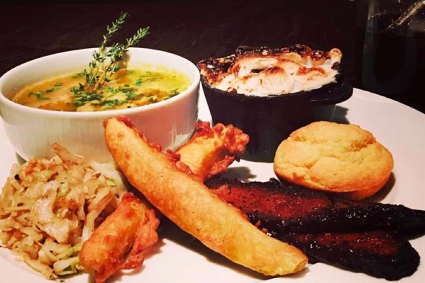 A plate with soup, cornbread, grilled meat, fried items, and cabbage.