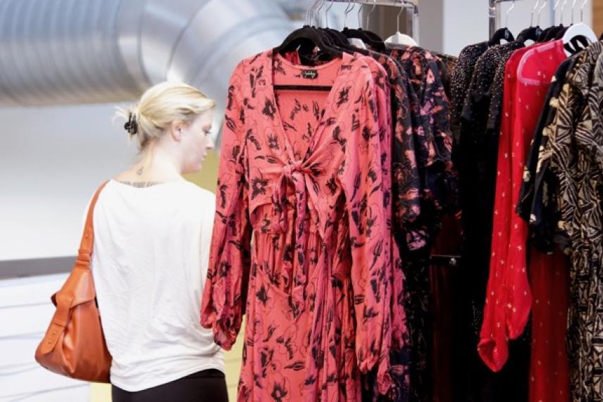 Blonde woman browsing vibrant printed dresses in a clothing store.
