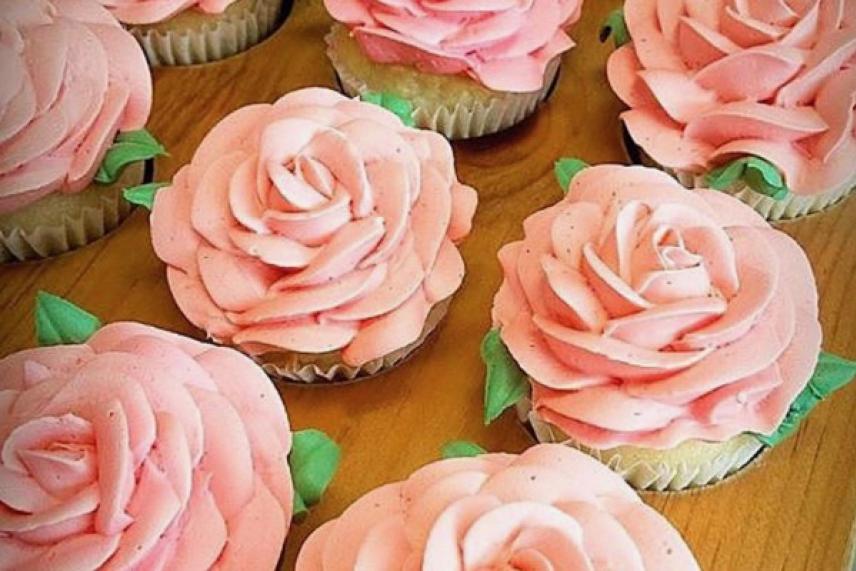 Pink rose cupcakes on a wooden surface.