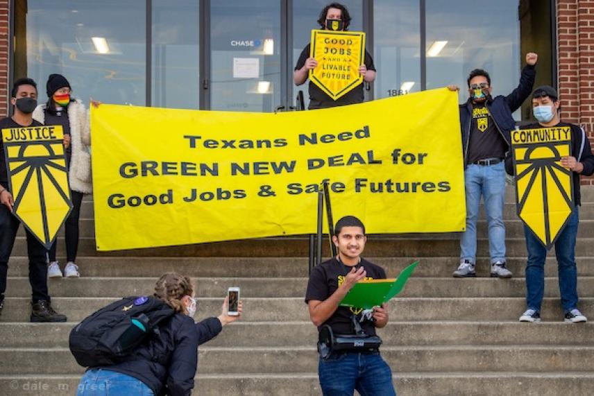 Protesters holding a yellow banner advocating for the Green New Deal on building steps.