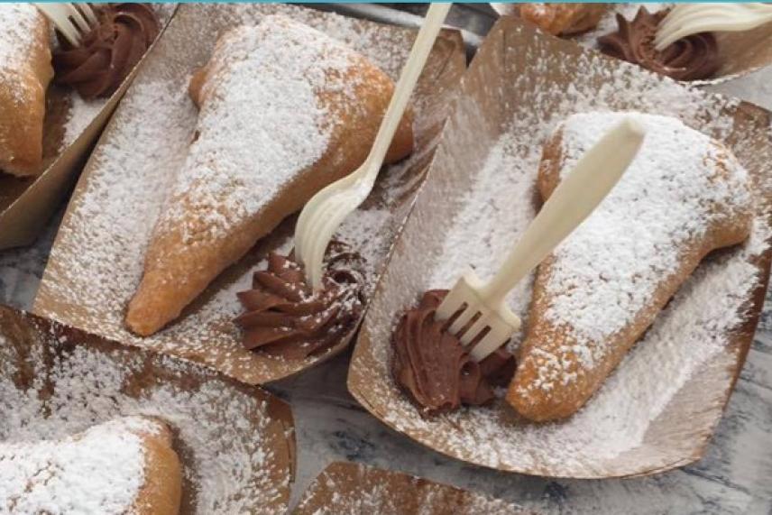 Pastries dusted with powdered sugar on paper trays with chocolate icing and forks.