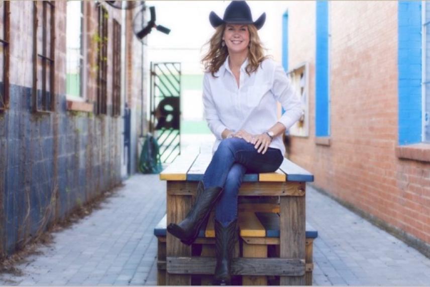 Woman in cowboy hat sitting on a picnic table in a colorful alley.
