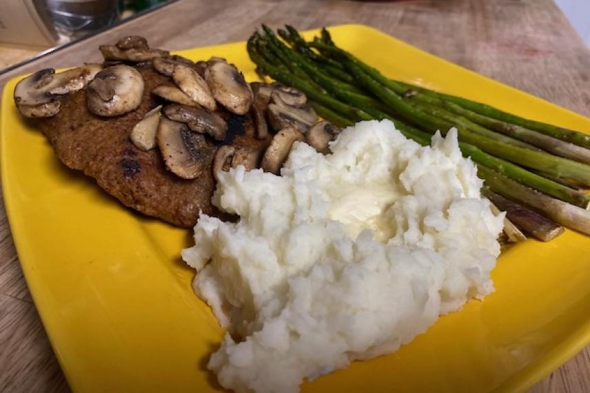 Steak with mushrooms, mashed potatoes, and asparagus on a yellow plate.