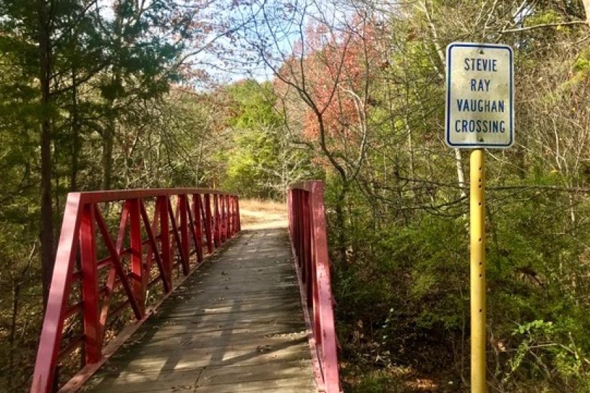 Red footbridge in a forested area with a pedestrian crossing sign.