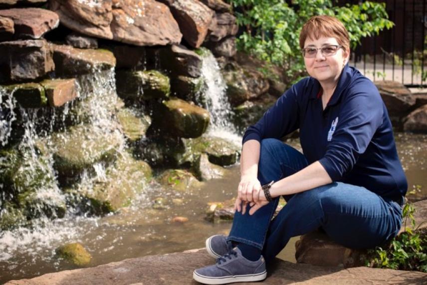 Seated person by a small waterfall in a garden setting, wearing a navy shirt and jeans.