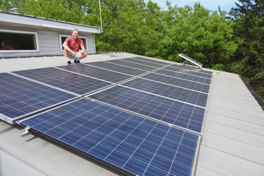 Roof with solar panels and a person kneeling beside them, surrounded by trees.