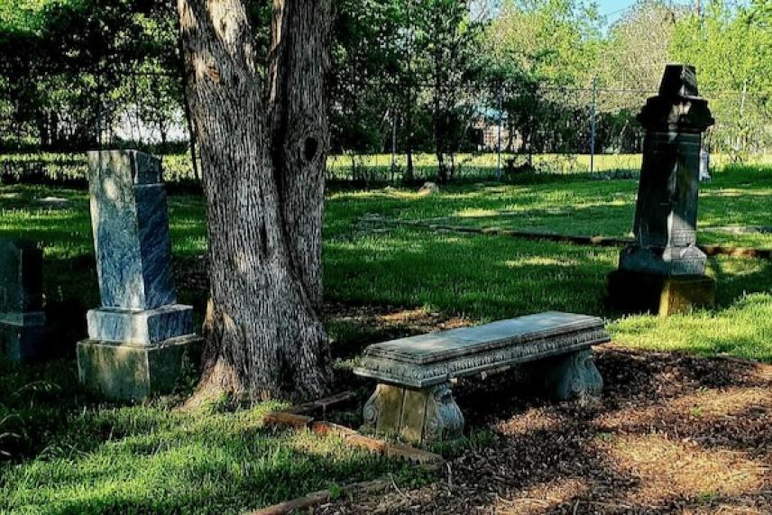 Grassy cemetery with tombstones, trees, and a stone bench.