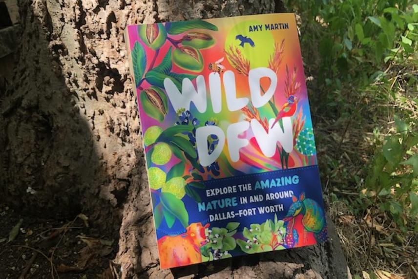 Colorful book titled "Wild DFW" leaning against a tree trunk.