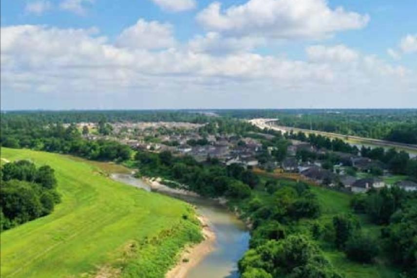 Lush landscape with a winding river, trees, and distant houses under a blue sky with clouds.