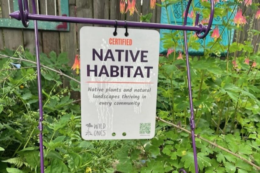 Sign labeled "Native Habitat" among lush greenery and flowers.