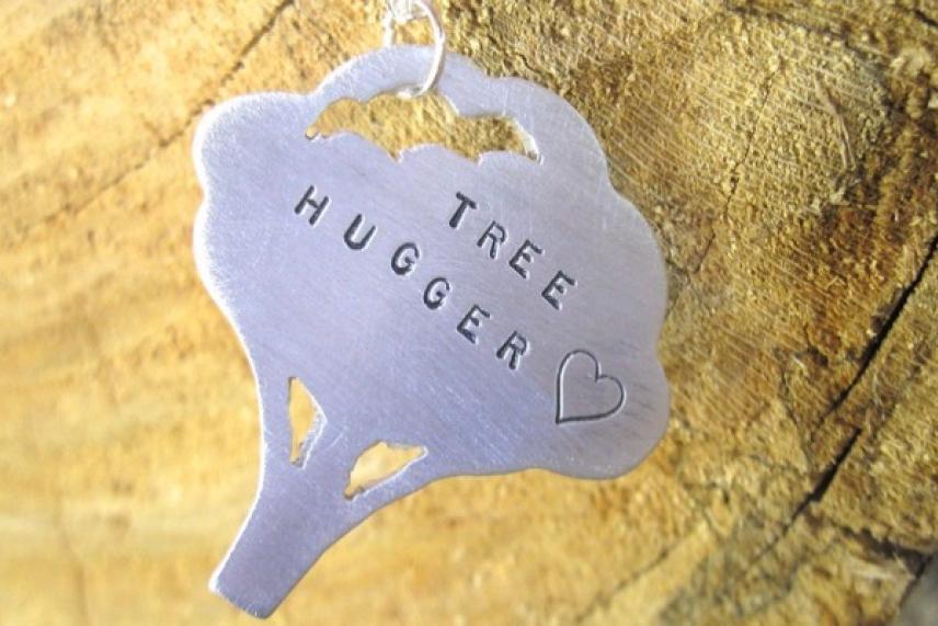 Pendant shaped like a tree on wood background, text reads "TREE HUGGER" with a heart.
