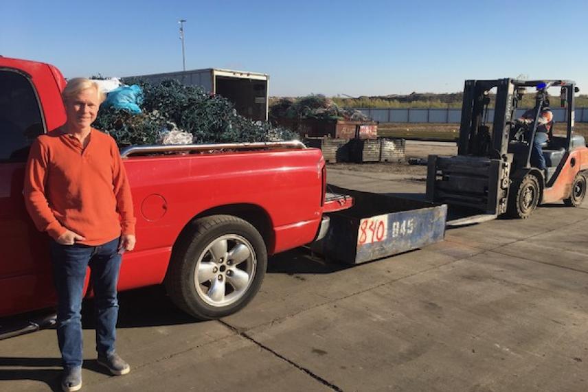 Man in orange sweater next to red truck by forklift, outdoor setting.