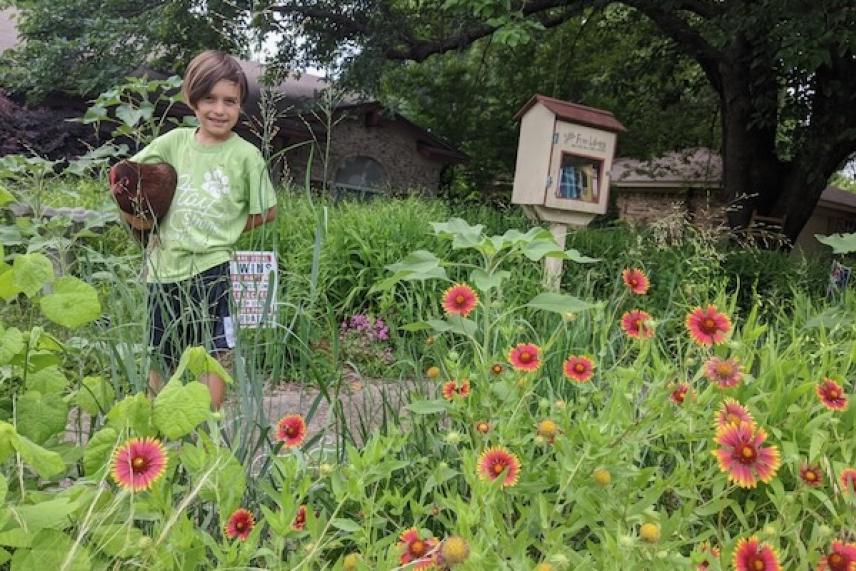 Child with a chicken in a garden of red flowers and green plants.