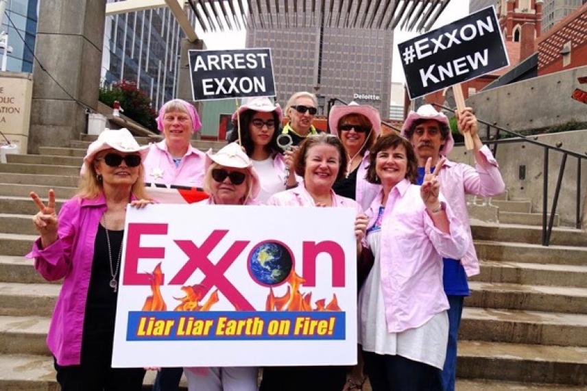 Protesters in pink attire, holding signs and a banner against Exxon.