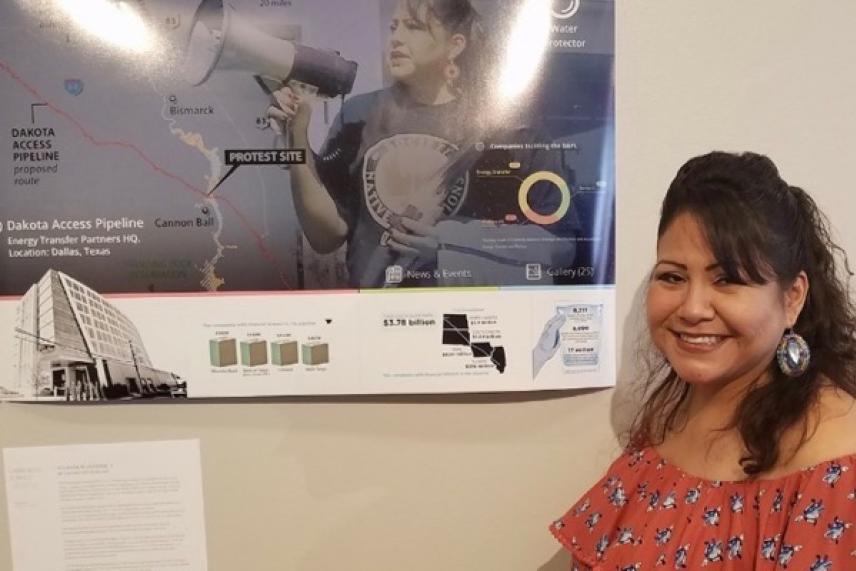 Smiling woman stands next to a collage with maps and diagrams on the wall.