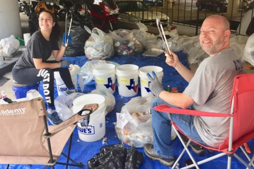 Sorting trash on a blue tarp, two people, smiling, holding tongs, surrounded by bags and buckets.