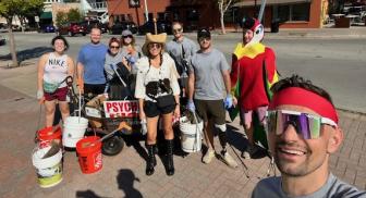 Group of people in playful costumes with cleaning supplies on a street.